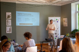 Lektors Elviss Brauns stāv kājās un rāda prezentāciju